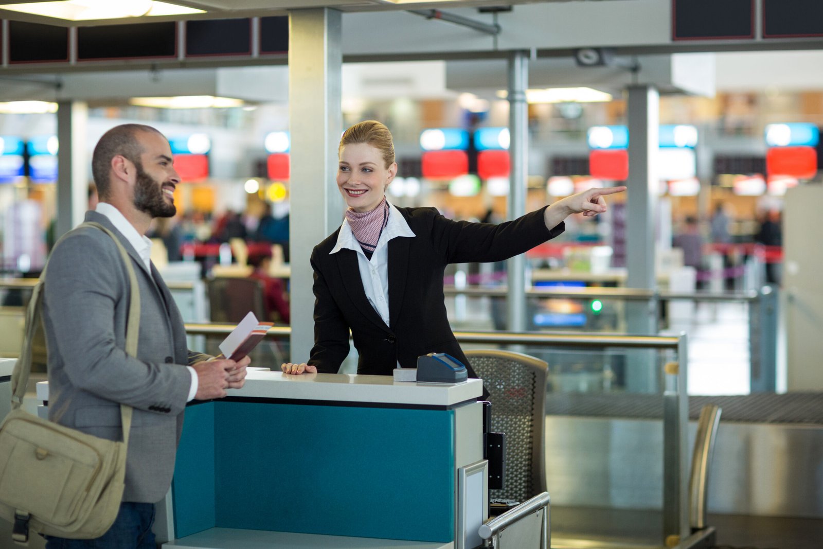 Airline check-in attendant showing direction to commuter at check-in counter in airport terminal